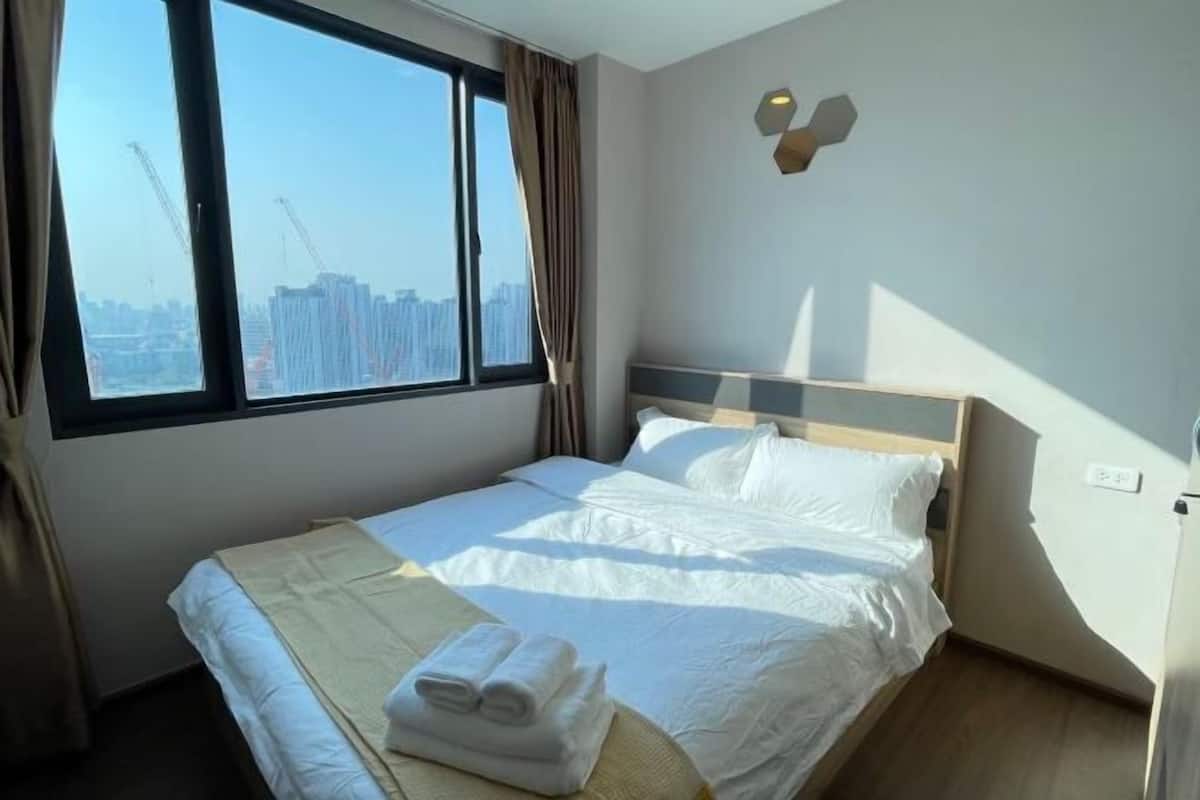 A hotel room with a large bed, a view of the cityscape, and a modern light fixture.