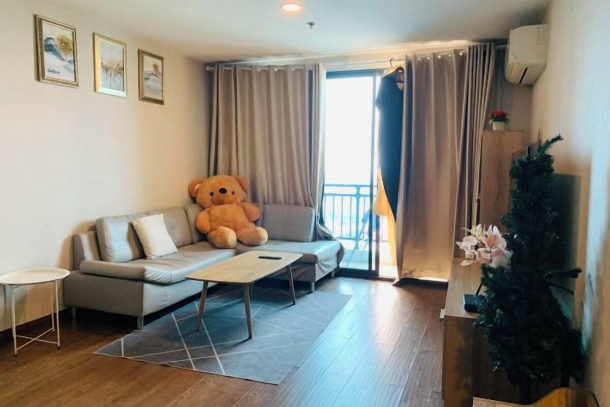 A living room with a sofa, a large teddy bear, a small table, and a potted plant.
