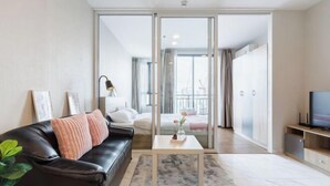 A modern living room with a black leather sofa, a small white table, and a TV on a wooden stand. - Artisan Ratchada Apartment Bangkok, Thailand (Bangkok)
