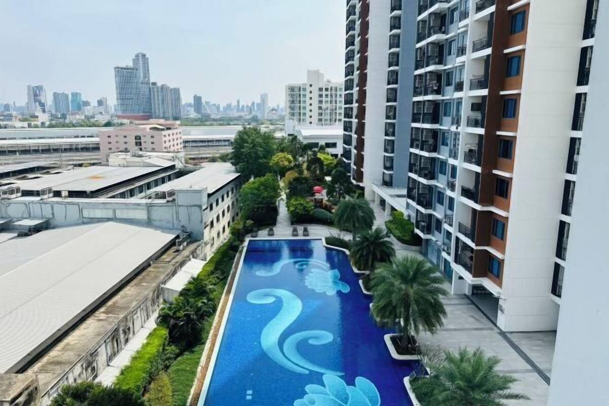 A residential building with a rooftop swimming pool, surrounded by greenery and high-rise buildings in the background.