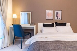 Une chambre d’hôtel avec un lit, un bureau, une chaise, une lampe et deux tableaux encadrés au mur.