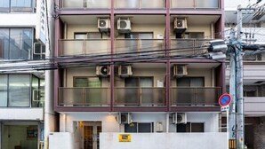 Ein mehrstöckiges Gebäude mit Klimaanlagen an jeder Etage, einem Verbotsschild und einer blauen Kiste davor.
