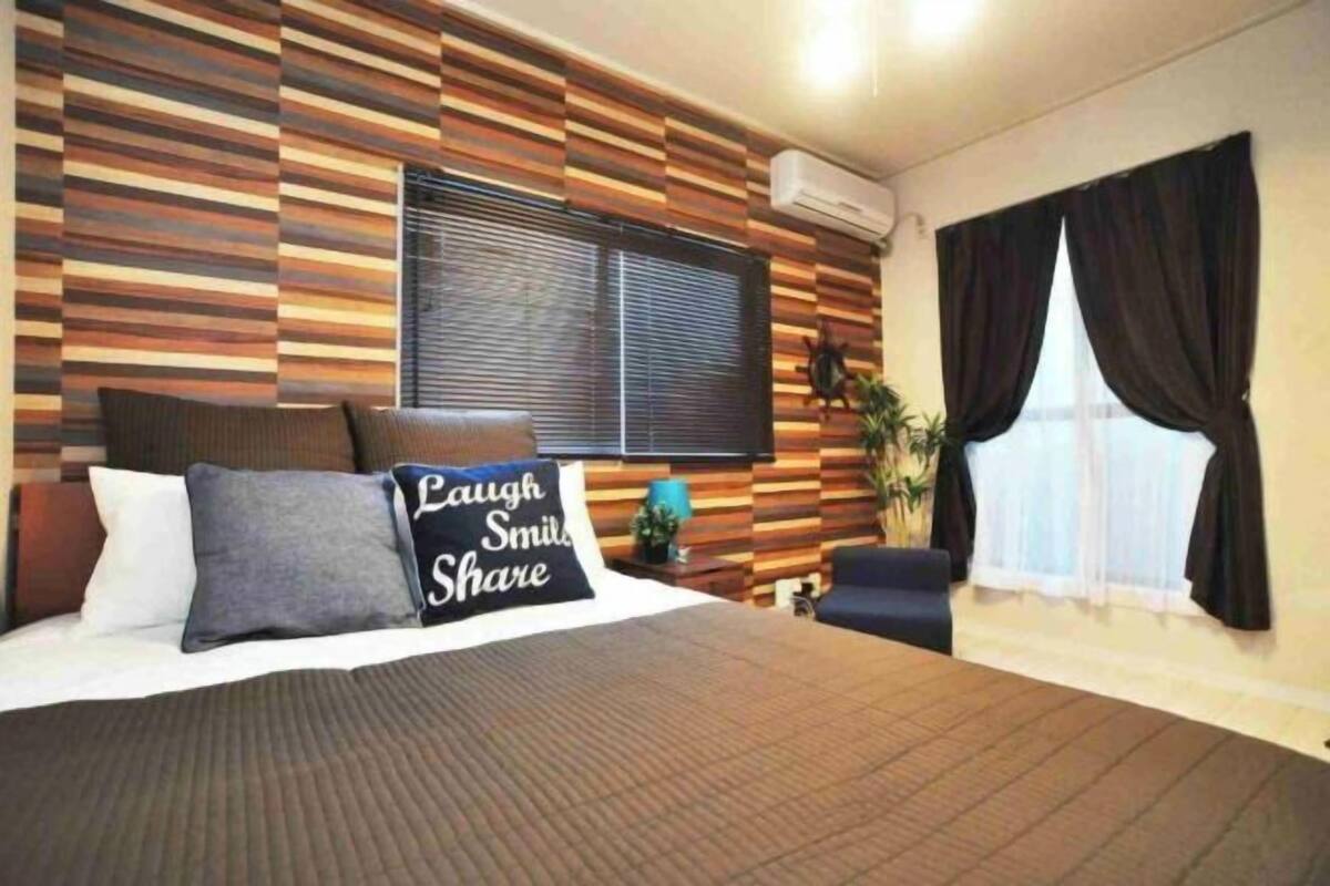 Une chambre d’hôtel avec un lit, une fenêtre avec des rideaux, un mur à motifs rayés et une petite table sur laquelle est posée une plante.