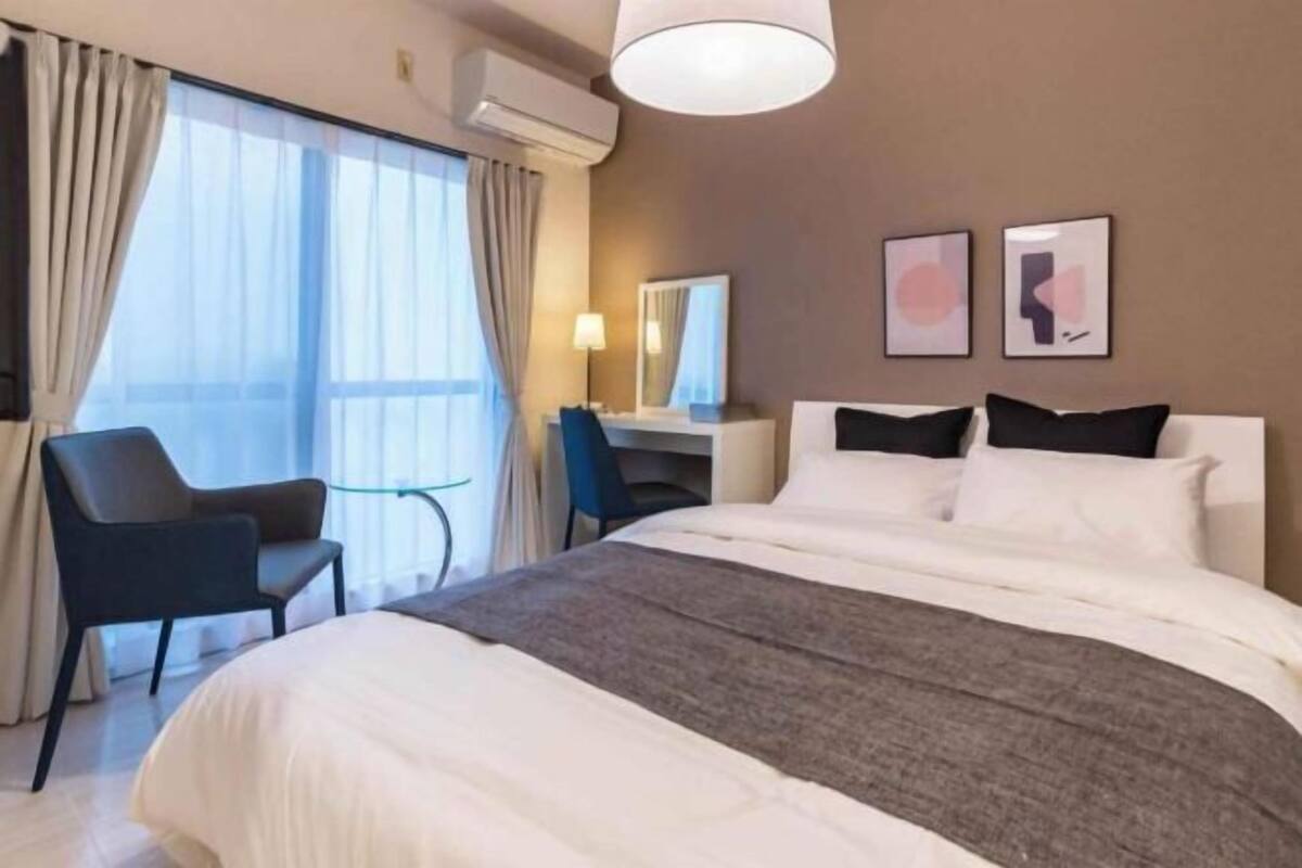 Une chambre d’hôtel avec un lit, un bureau, une chaise et une grande fenêtre.