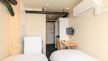 Habitación de hotel compacta con dos camas individuales, una kitchenette pequeña, un televisor montado en la pared y un equipo de aire acondicionado instalado en el techo.
