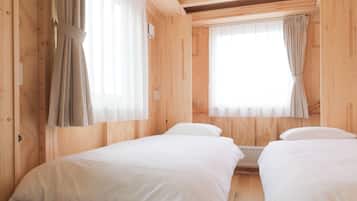 Una habitación con dos camas, paredes de madera y ventanas grandes con cortinas ligeras.