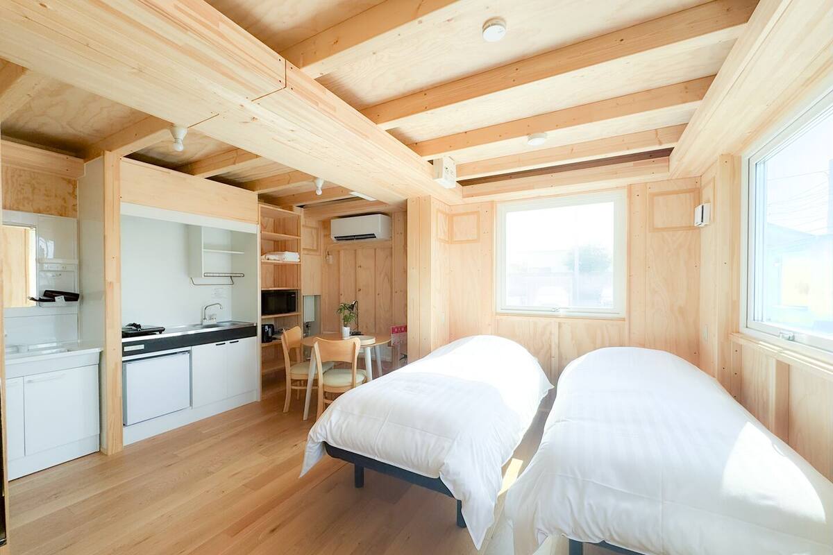 Una habitación compacta con kitchenette, dos camas, una mesa de comedor y un ventanal.