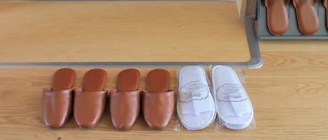 A wooden floor with a mat, a shoe rack with brown and white shoes, and a pair of slippers.