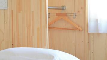 A wooden room with a bed, a wooden hanger, and a window with curtains.