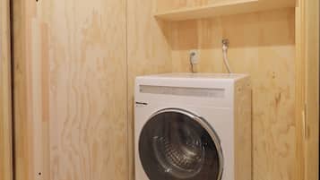 A compact, wooden-walled laundry room with a built-in front-loading washing machine.