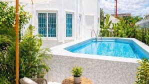 A swimming pool with a white tiled wall, a wicker chair, and a small table with a plant. - tropical private pool villa (Bangkok)