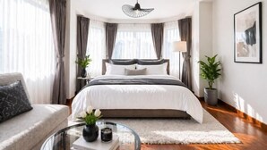 A modern bedroom with a large bed, a sofa, a glass coffee table, and a ceiling fan. - tropical private pool villa (Bangkok)