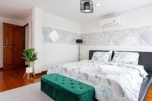 A bedroom with a bed, a green ottoman, a potted plant, and a wall-mounted air conditioner. - tropical private pool villa (Bangkok)