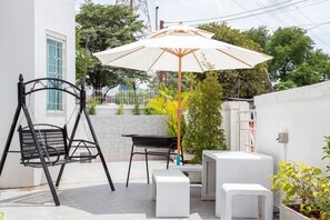 A patio area with a swing chair, a table, a white chair, and a large umbrella. - tropical private pool villa (Bangkok)