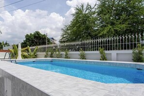 A swimming pool with a white tiled edge, surrounded by a white fence, and trees in the background. - tropical private pool villa (Bangkok)