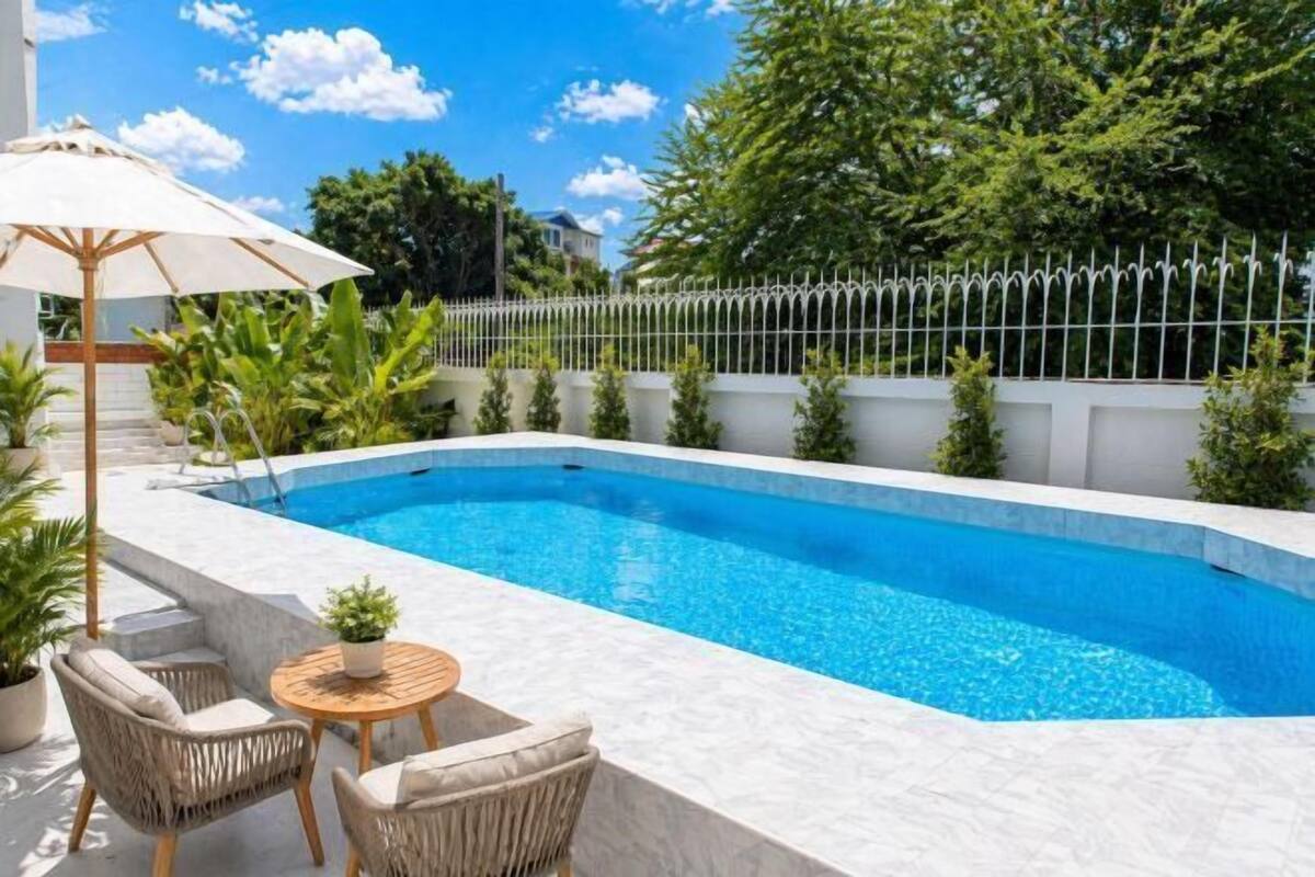 A swimming pool with a white fence, outdoor furniture, and potted plants.