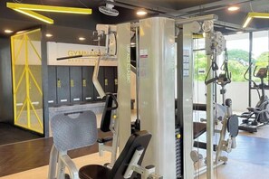 Une salle de sport équipée de matériel d’exercice, de casiers et offrant une vue sur la verdure environnante.