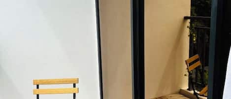 Un balcon avec un banc en bois et une chaise, un sol carrelé et une vue sur la verdure environnante.