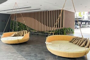 Un hall d’entrée moderne avec deux canapés suspendus en osier et un mur composé de lattes de bois disposées verticalement.
