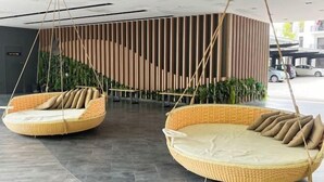 Dos sillas colgantes de mimbre con cojines en un vestíbulo moderno con una pared de madera curva y piso de baldosas.