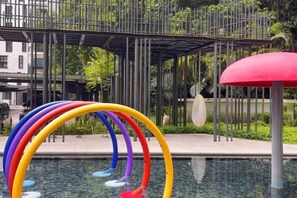 Un espace piscine agrémenté de plusieurs anneaux colorés et d’un parasol rouge.