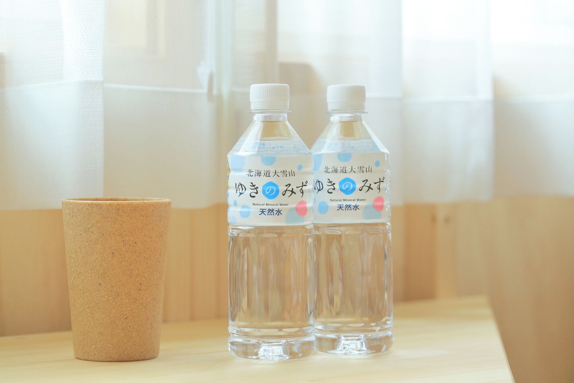 Two bottles of water and a cork mug on a wooden surface.