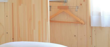 A wooden room with a bed, a wooden hanger, and a window with curtains.