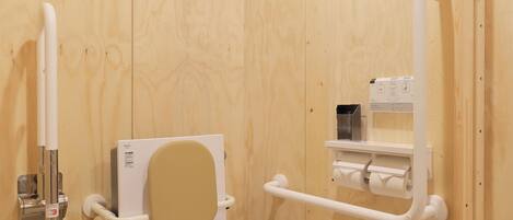 Un baño de madera con inodoro blanco, dispensador de desinfectante de manos y baranda.