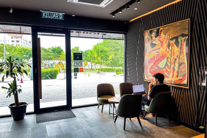 A hotel lobby with a reception desk, seating area, and a large window offering a view of the street.