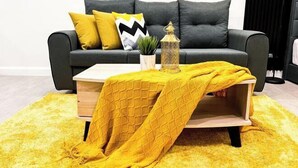 Ein modernes Wohnzimmer mit einem grauen Sofa, gelben Kissen, einem Holztisch und einer gelben Decke.