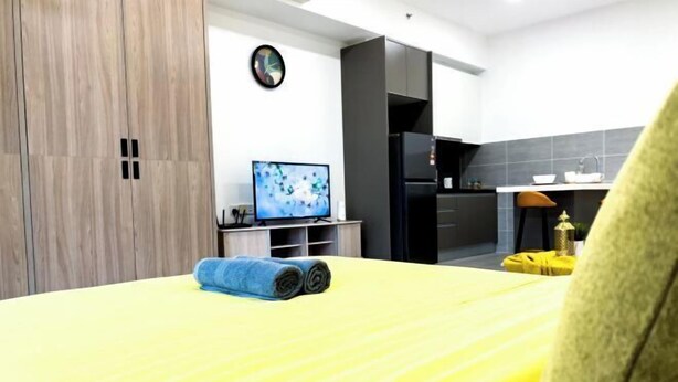 Ein modernes Hotelzimmer mit einem Bett, einem Fernseher, einem kleinen Tisch und einer Küchenzeile.