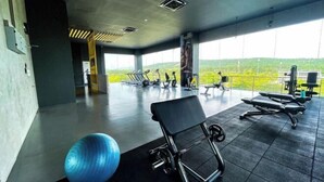 Ein Fitnessraum mit Trainingsgeräten, einem blauen Trainingsball und großen Fenstern mit Blick auf Grünflächen.