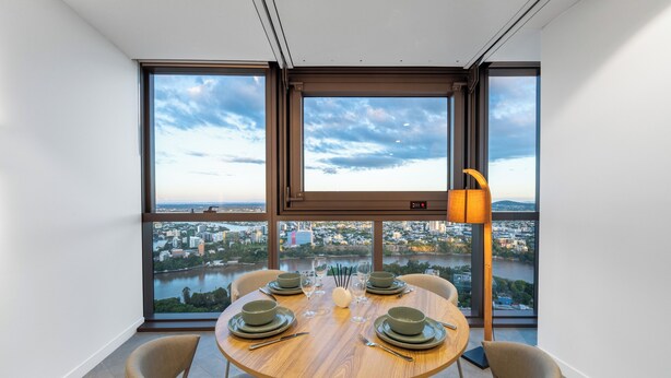 A dining area with a round table set for four, large windows offering a city view, and a modern floor lamp.