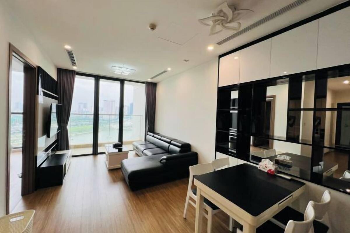 Sala moderna com sofá preto, mesa de jantar com cadeiras e uma grande janela com vista para a cidade.