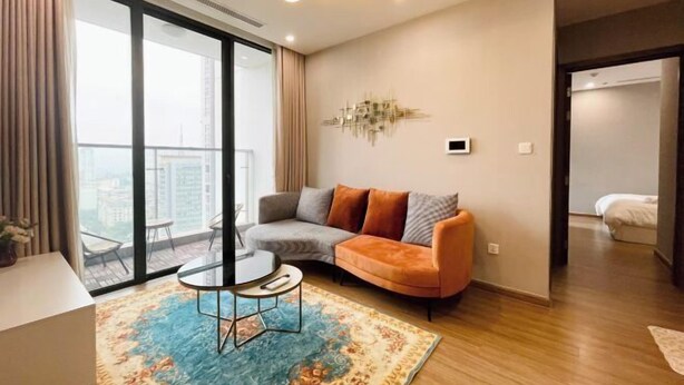 A modern living room with a sofa, a coffee table, a chandelier, and a large window. - Vinhomes Skylake Premier Residence Ha Noi - Marina Housing (Hanoi)