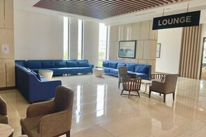 Un espace détente avec des canapés et des fauteuils, un sol carrelé et un panneau indiquant l’entrée du salon.