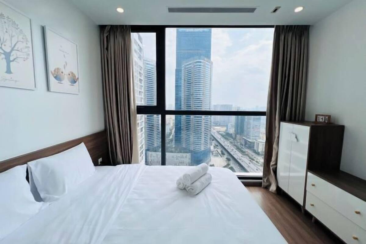 Quarto de hotel com cama grande, guarda-roupa, janela com vista para a cidade e duas imagens emolduradas na parede.
