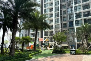 Un bâtiment moderne doté d’un terrain de jeux, de palmiers et d’un jardin bien entretenu.