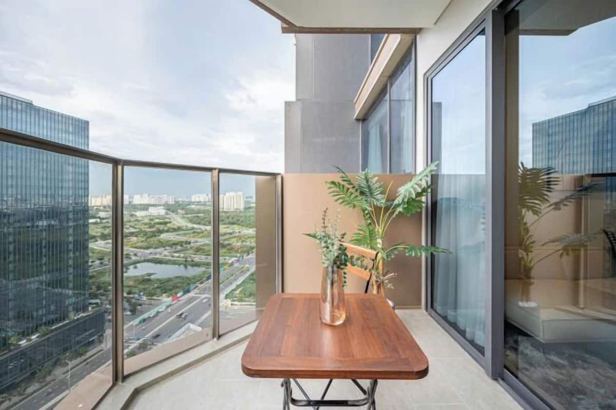 Un balcon avec une table en bois et des plantes en pot, offrant une vue sur le paysage urbain et sur une étendue d’eau.