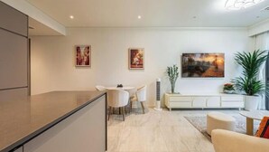 A modern kitchen with a dining area, featuring a white countertop, a dining table with chairs, and a large painting on the wall. - The Metropole Signature Collection – Galleria, Crest & Opera (Ho Chi Minh City)