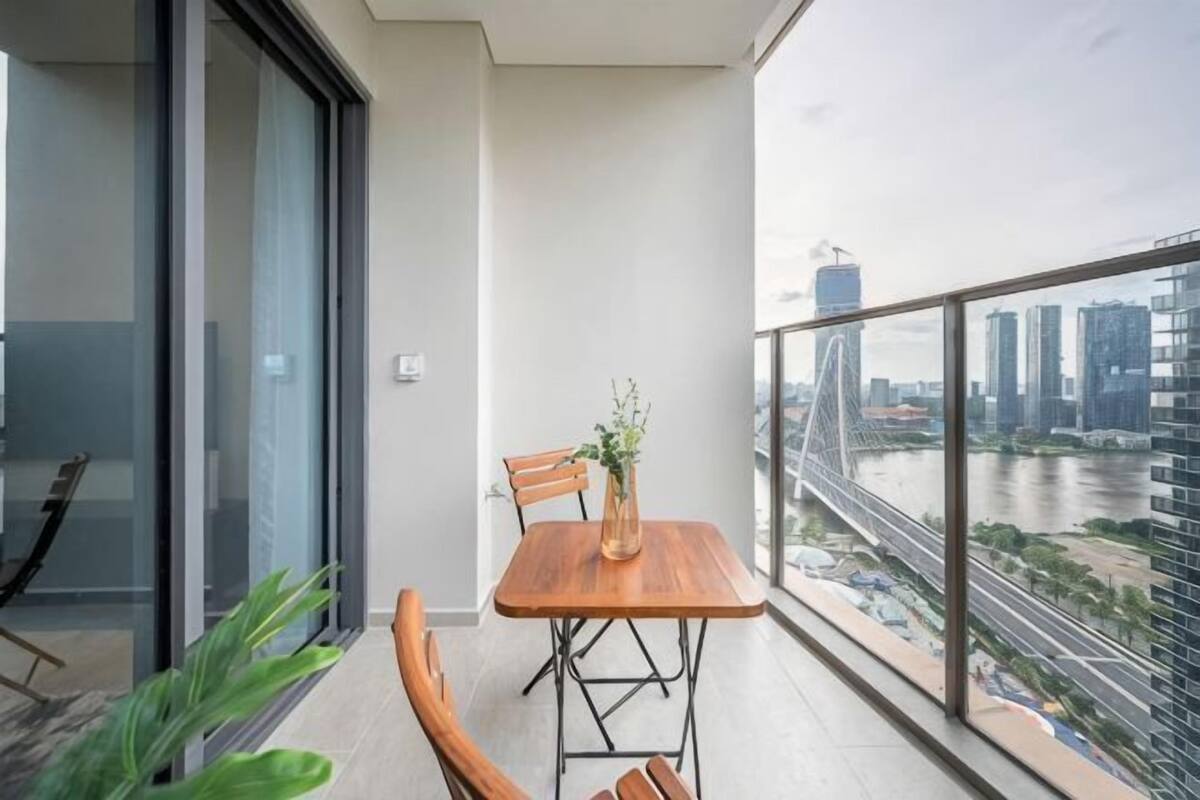 Un balcon avec une table et des chaises, une vue sur le paysage urbain et la rivière, et une porte vitrée donnant sur un espace intérieur.