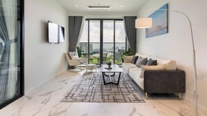 A modern living room with a sofa, coffee table, and chairs, large windows with a city view, and a painting on the wall. - The Metropole Signature Collection – Galleria, Crest & Opera (Ho Chi Minh City)