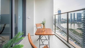A balcony with a table and chairs, a vase with a plant, and a view of a cityscape and river. - The Metropole Signature Collection – Galleria, Crest & Opera (Ho Chi Minh City)