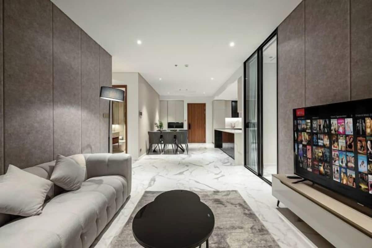 Un salon moderne avec un canapé, une table basse noire, un téléviseur à écran plat et, au fond, un coin repas.