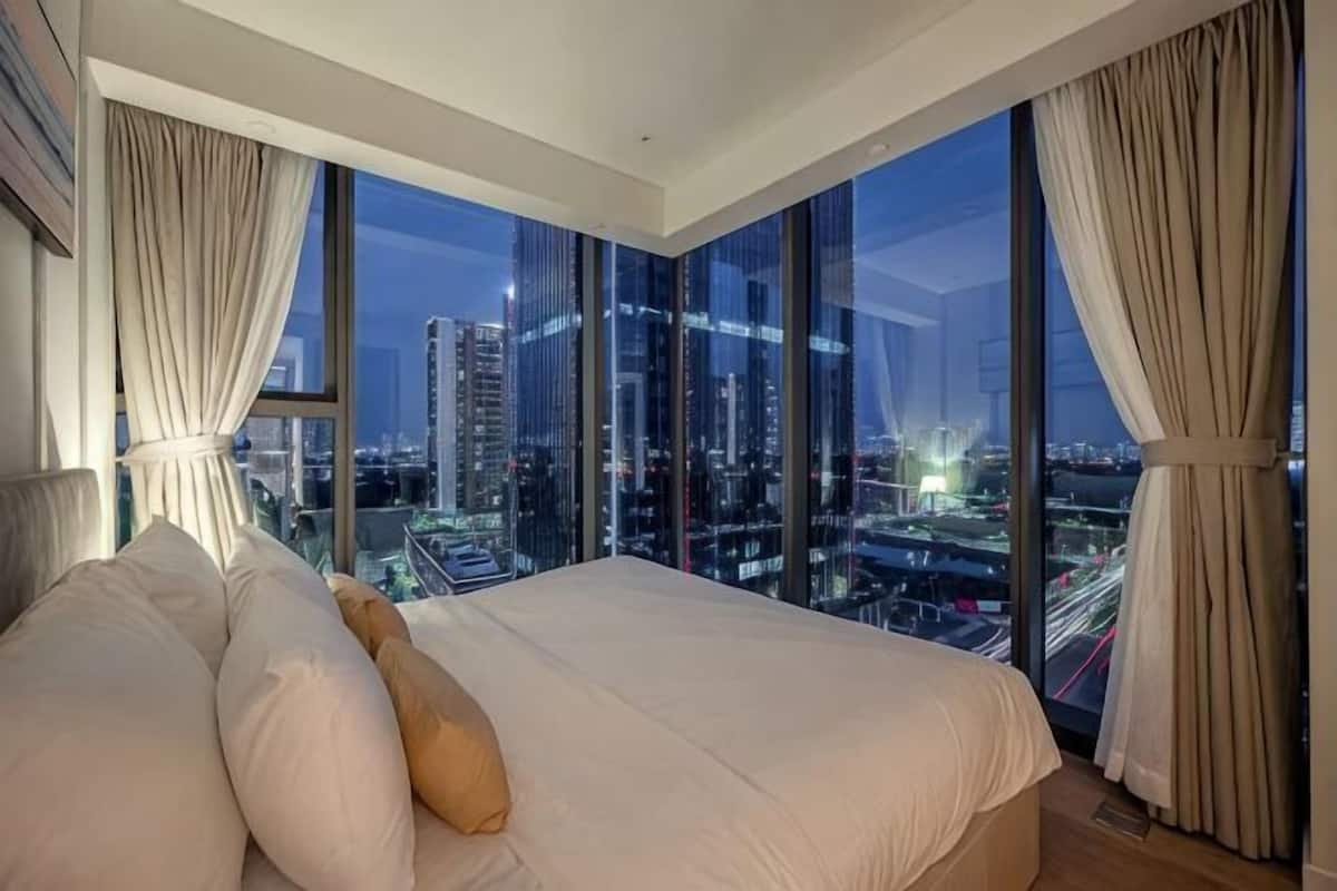 Une chambre avec un grand lit, une vue sur la ville et des rideaux.