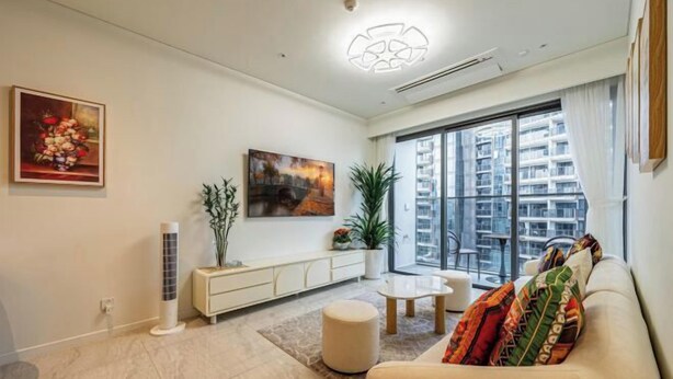 A modern living room with a sofa, a coffee table, a sideboard, a potted plant, and a large window with a view of high-rise buildings. - The Metropole Signature Collection – Galleria, Crest & Opera (Ho Chi Minh City)