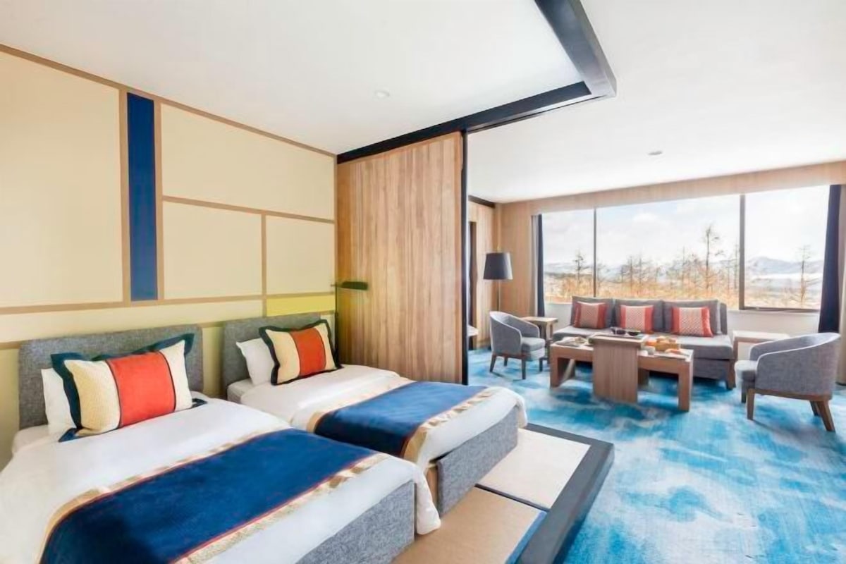 Habitación de hotel con dos camas, un sofá, una mesita de centro y un ventanal con vistas.