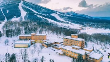 A snow-covered resort with multiple buildings, a ski slope in the background, and a mountainous landscape.
