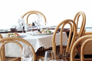 A dining table with chairs, a white tablecloth, and a view of the sea.