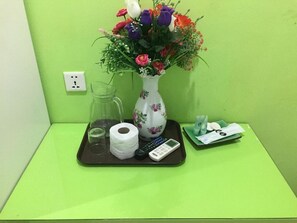 A green wall with a vase of flowers, a glass pitcher, a roll of toilet paper, a remote control, and a tray with tissues and a small box. - Swing & Pillows @ KL Pekeliling (Kuala Lumpur)